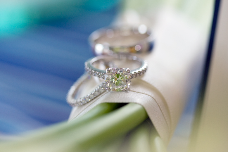A beautiful diamond engagement ring rests on a classic white calla lily wedding bouquet.