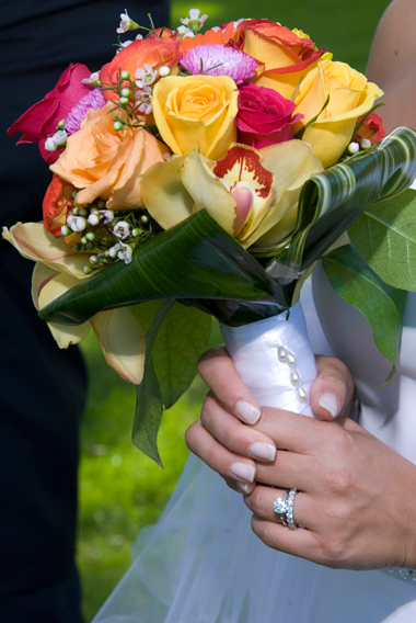 A summer wedding bouquet consisting of multi-colored roses, orchids and gerbera daisies with a white ribbon handle and pearl accents.