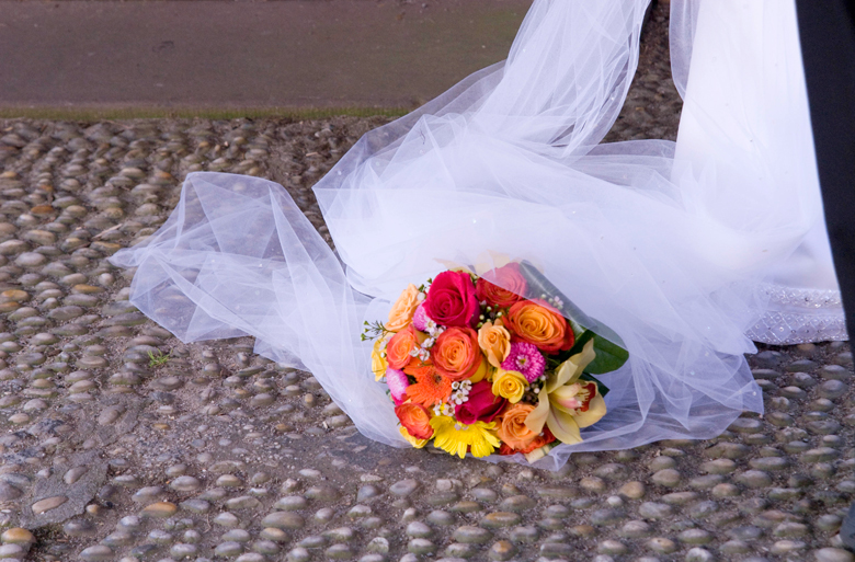 A summer wedding bouquet consisting of multi-colored roses, orchids and gerbera daisies is resting on the bride's tulle veil.