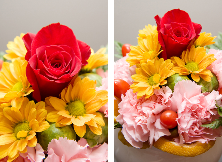 A centerpiece consisting of a red rose, yellow daisies, pink carnations, and brussel sprouts.