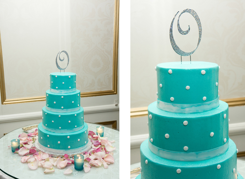 A beautiful turquoise blue wedding cake with white polka dots and a rhinestone cake topper surrounded by pink rose petals and votive candles.