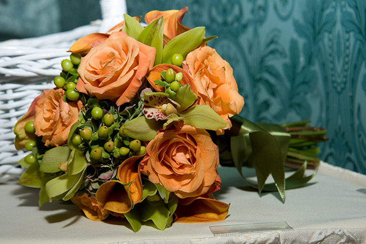 An autumn wedding bouquet consisting of peach roses, coral calla lilies, orchids and green berries. The bouquet's handle is wrapped in a pretty chartreuse ribbon.