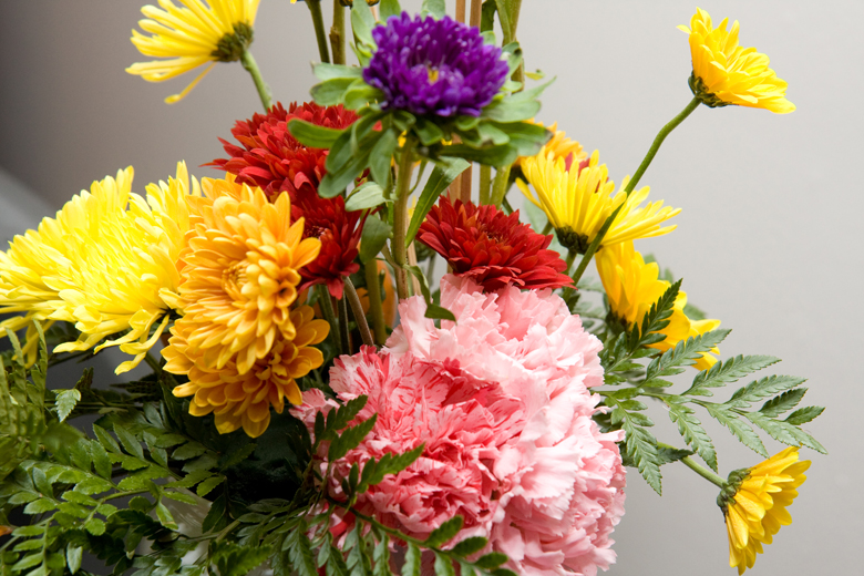 A centerpiece consisting of yellow, orange, purple and maroon chrysanthemums and pink carnations.