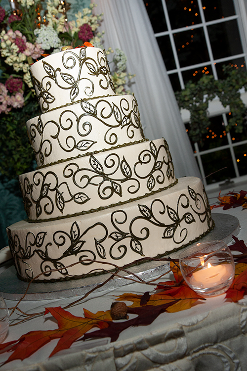 A beautiful four-tiered, filigree, wedding cake surrounded by autumn leaves, acorns and votive candles.