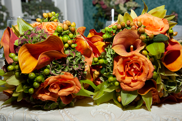An autumn wedding bouquet consisting of peach roses, coral calla lilies, orchids and green berries.